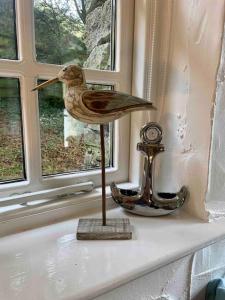 una estatua de un pájaro de madera sentada en una cornisa de la ventana en Grooms cottage, a tranquil Cornish retreat en Lanteglos