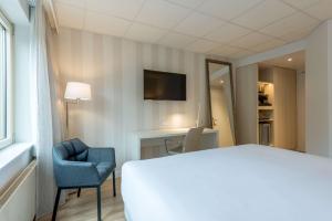 um quarto de hotel com uma cama e uma cadeira e uma televisão em NH Eindhoven Conference Centre Koningshof em Veldhoven