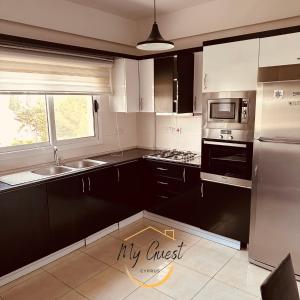 a kitchen with black and white cabinets and a refrigerator at 2-Bedroom Apartment Pamfilya 7 by MyGuest Cyprus in Famagusta