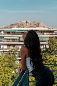 Una donna seduta su una panchina di fronte a un edificio di Athesense Suites ad Atene