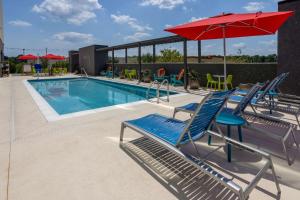 a swimming pool with blue chairs and a red umbrella at Tru By Hilton Pensacola Airport Medical Center in Pensacola
