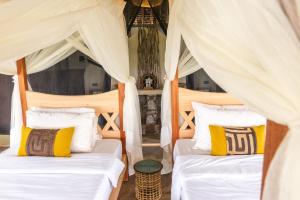 two beds in a room with white curtains and yellow pillows at Soroi Cheetah Tented Camp in Mwatate