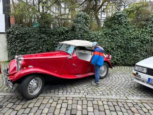 a man is standing next to a red car at Ferienwohnung im Resi Gesundheitszentrum in Freudenberg