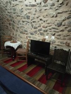 Habitación con pared de piedra, TV y mesa. en Ο ΘΟΛΟΣ en Stemnitsa