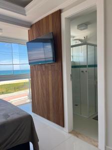 a bedroom with a glass shower with a television on a wall at Triplex Vista Azul in Rio das Ostras