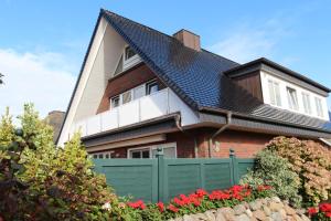 une maison avec une clôture verte et des fleurs rouges dans l'établissement Haus Günther - Mittelweg 1, App 2, à Wenningstedt