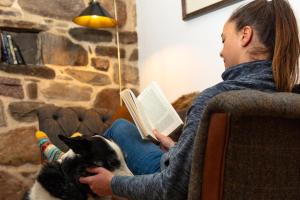 una mujer sentada en un sofá leyendo un libro con un gato en The Ruin - Lochside Cottage dog friendly, en Ullapool