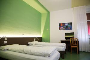three beds in a room with green walls and a chair at Hotel Villa Flora in Roncegno