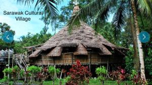 a small hut with a thatched roof next to a palm tree at Riverview Home @Waterfront KCH in Kuching