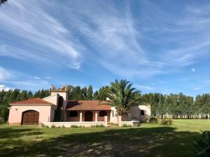 ein Haus auf einem grasbewachsenen Feld mit Bäumen im Hintergrund in der Unterkunft Casaquinta Haras El Tropicano in Bahía Blanca