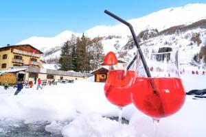 two wine glasses sitting in the snow in front of a mountain at Hotel Arlecchino - Dada Hotels in Madesimo
