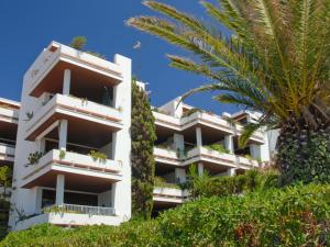 a white apartment building with a palm tree at Apartamentos del Rey in Portinatx