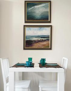 a white table with two chairs and two paintings on the wall at Villa Ariane in Saint-Valery-en-Caux