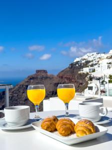 una mesa con dos vasos de zumo de naranja y bollería en Reverie Santorini Hotel, en Firostefani