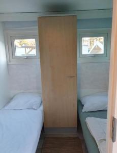Het kleine huis في Schoonloo: سريرين في غرفة صغيرة بها نافذتين