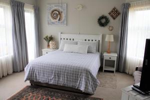 1 dormitorio con 1 cama con colcha blanca y ventanas en The Sun Catcher B&B, en Struisbaai