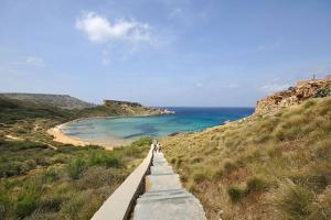 two people walking down a path towards a beach at Seaside Serenity - A lovely apartment with views in Mellieħa