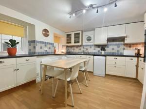 een keuken met witte kasten en een tafel en stoelen bij Beautifully decorated bright and cosy cottage in Aveton Gifford