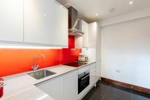 una cocina con armarios blancos y una pared de color naranja en Colourful South Kensington Home, en Londres
