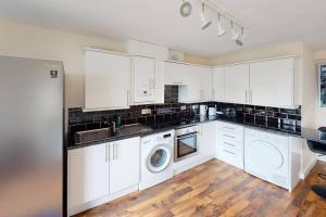 cocina con armarios blancos, lavadora y secadora en Lovely two bed flat with free parking (4 117) en Nottingham