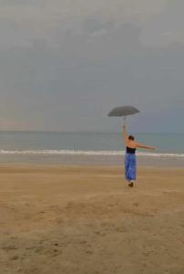 EJ'S House/ Room في Dulag: امرأة تمشي على الشاطئ وهي ممسكة بمظلة