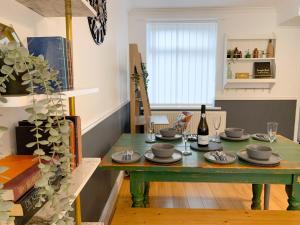 een eetkamer met een groene tafel met borden en wijnflessen bij Cosy 3 bed home with garden - near to uni, restaurants & bars in Hull