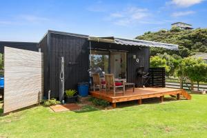 une petite maison noire avec une terrasse en bois dans l'établissement Pacific Bay HQ - Tutukākā Holiday Unit, à Tutukaka