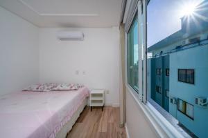 1 dormitorio con cama y ventana grande en Aluguel Apartamento 3 quartos sendo 1 suíte em Bombinhas, en Bombinhas