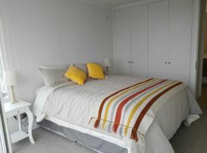 Dormitorio blanco con cama con almohadas amarillas en Departamento playa La Herradura en Coquimbo