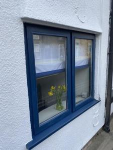 une fenêtre bleue avec un vase orné de fleurs jaunes. dans l'établissement 1750's cottage with open fire and beams, à Upholland