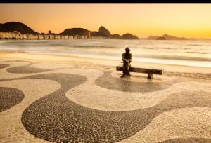 Loft Praia de Copacabana في ريو دي جانيرو: شخص يجلس على مقعد على الشاطئ