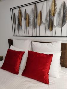 Cama blanca con almohadas rojas y plumas en la pared en Apartman Modiano en Vrnjačka Banja