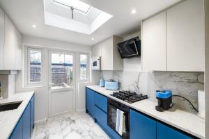 een keuken met blauwe en witte kasten en een fornuis bij Luxurious 2 bedroom flat with parking and garden, 5 mins walk to train station and bus stop opposite property in Londen