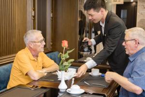 zwei Männer sitzen an einem Tisch in einem Restaurant mit einem Kellner in der Unterkunft Minasi Premium Hotel in Hanoi