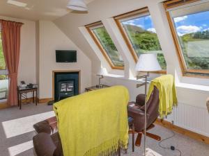una sala de estar con una manta amarilla en una silla y ventanas en The Barn, en Dalmally
