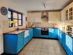 a blue kitchen with white cabinets and a sink at Cobweb Cottage in Ludham