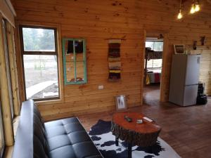 Sala de estar de una cabaña de madera con mesa y nevera en Rukawe Quillon, en Quillón