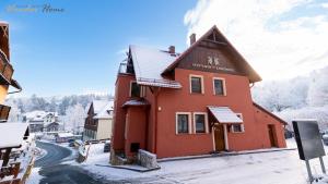 un edificio rosso su una strada con la neve sul terreno di Wonder Home - Apartamenty Karkonosz blisko wyciągów narciarskich, szlaków i restauracji a Karpacz
