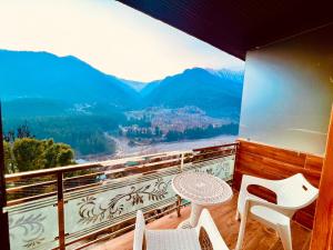uma varanda com mesa, cadeiras e montanhas em Bentenwood Resort - A Beutiful Scenic Mountain & River View em Manali