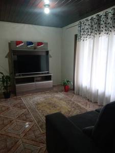 een woonkamer met een flatscreen-tv en gordijnen bij Casa linda e aconchegante para hóspedes.(Studio) in Joinville