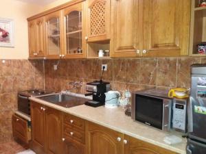cocina con armarios de madera, fregadero y microondas en Стаи за гости Анхиало en Pomorie