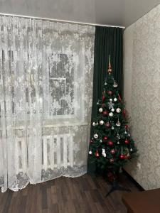 a christmas tree in a living room next to a curtain at 5 мин международный аэропорт in Prigorodnyy