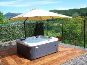 uma banheira de hidromassagem com um guarda-sol num deque de madeira em Flat with heated hot tub and shared pool em Casola in Lunigiana