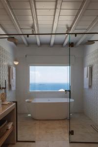Birdhouse Private Luxury Suite في أغيوس يوانيس ميكونوس: حمام مع حوض استحمام و نافذة كبيرة