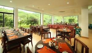uma sala de jantar com mesas e cadeiras e janelas grandes em Hotel C7 Munnar em Munnar