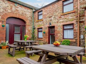 two wooden picnic tables in front of a brick building at 1 Bed in Gamblesby 90416 in Kirkoswald