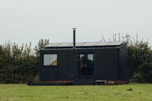 a black tiny house sitting in a field at Re Cabins - Reconnect Cabin - St Albans 