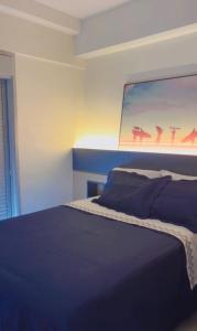 a bedroom with a blue bed with a painting on the wall at Flat vista mar em Santos in Santos