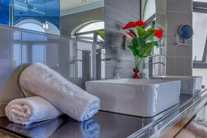 baño con lavabo y jarrón con flores rojas en Villa Tasha Luxury Suites, Lanseria, en Johannesburgo