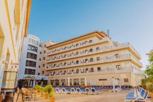a large hotel with lounge chairs and a building at Hotel Monarque Costa Narejos in Los Alcázares